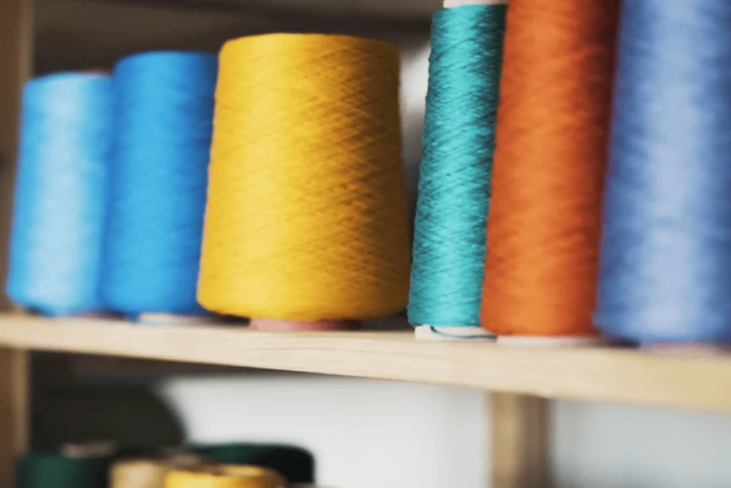 Large spools of thread in yellow, blue, turquoise, and orange are arranged on a wooden shelf.