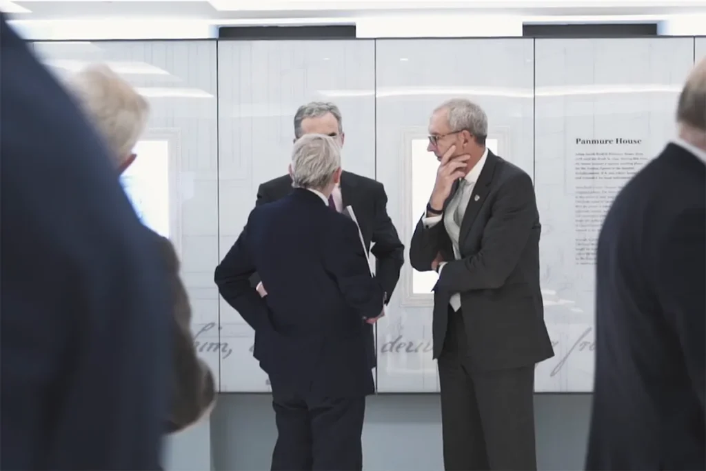 Three men engage in conversation at an exhibition, showcasing a modern interior with informational displays in the background.