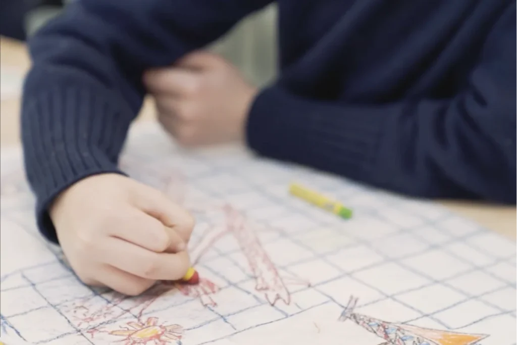 Child draws with red coloured pencil on chequered paper