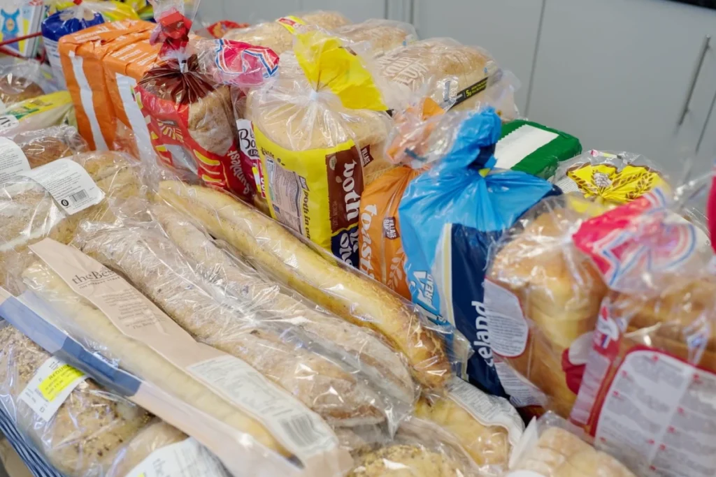 An assortment of various bread loaves and rolls packaged in plastic, displayed on a table in a grocery store.