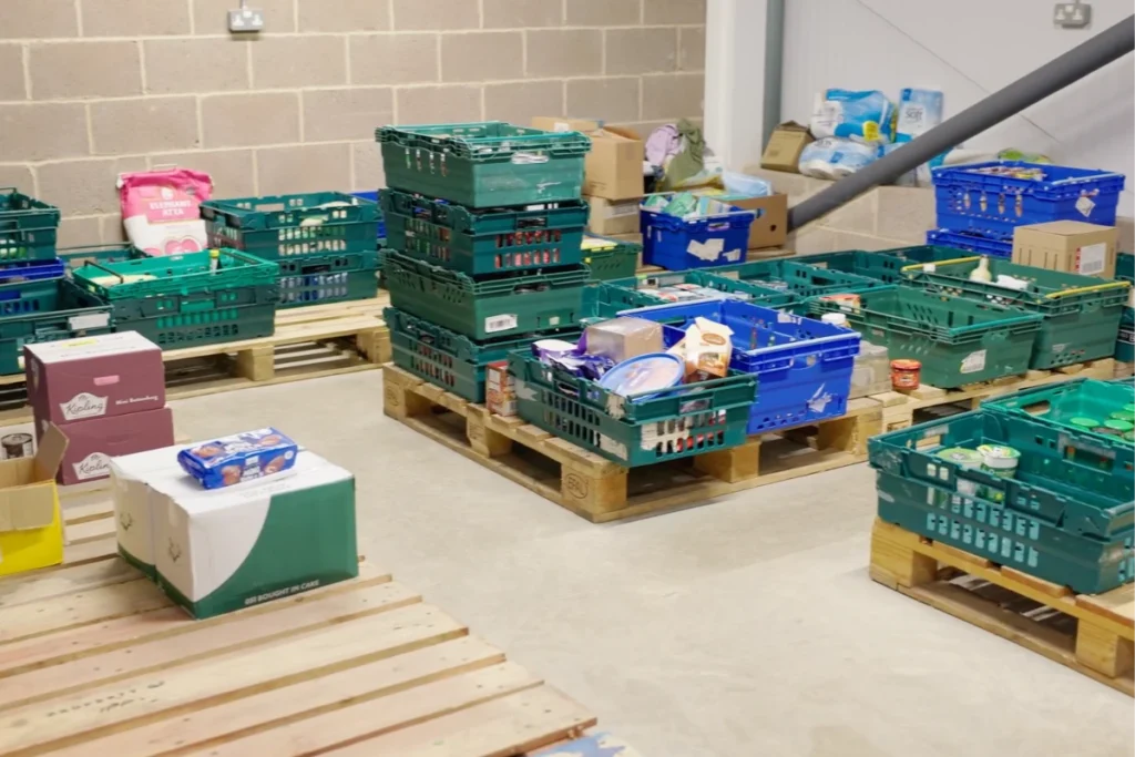 A food storage area with stacked crates filled with various food items and supplies on wooden pallets.
