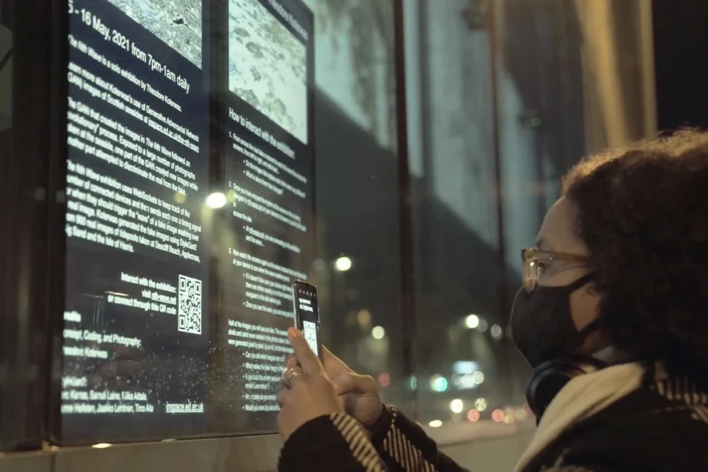 A person interacts with a digital exhibition display, capturing information with a smartphone while wearing a mask at night.