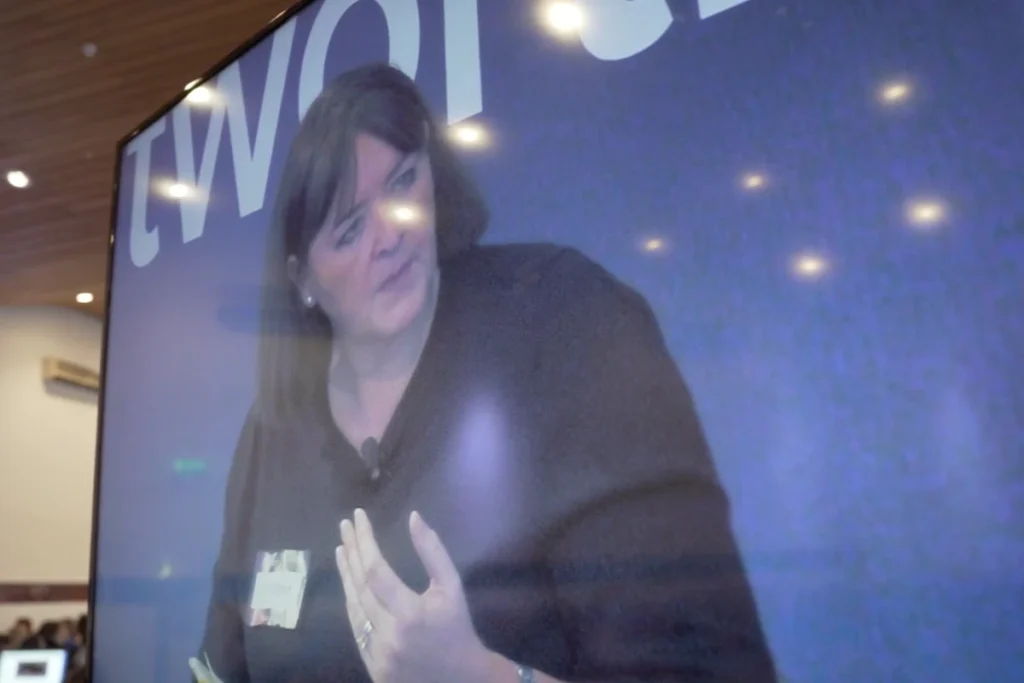 A woman speaking passionately at the Scottish AI Summit Promotional, captured on a large screen, showcasing her engagement with the audience.