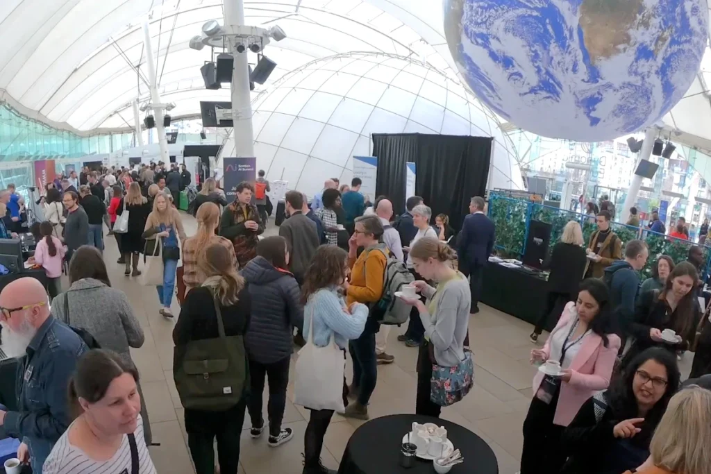 At the Scottish AI Summit Promotional event with diverse attendees networking and engaging in discussions under a large dome structure with an Earth globe display.