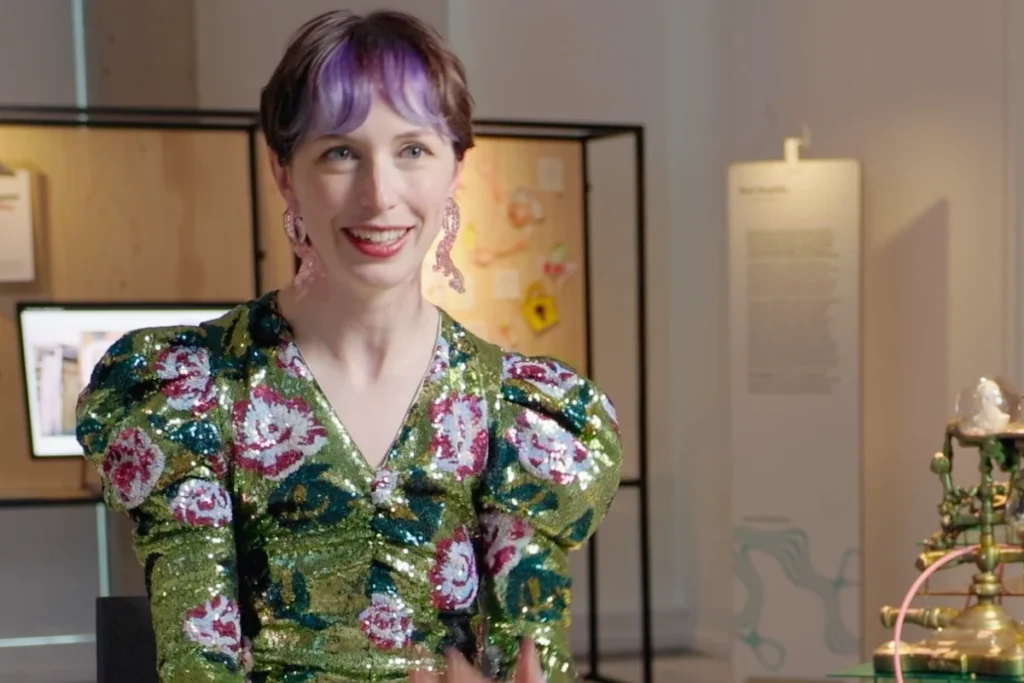 Artist Rachel McLean, sitting leaning forwards, wearing a sparkly outfit